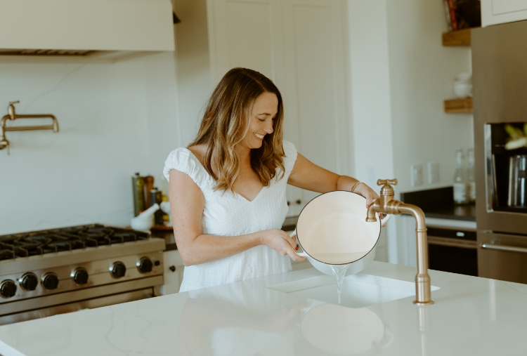 mujer drena olla en lavabo de cocina