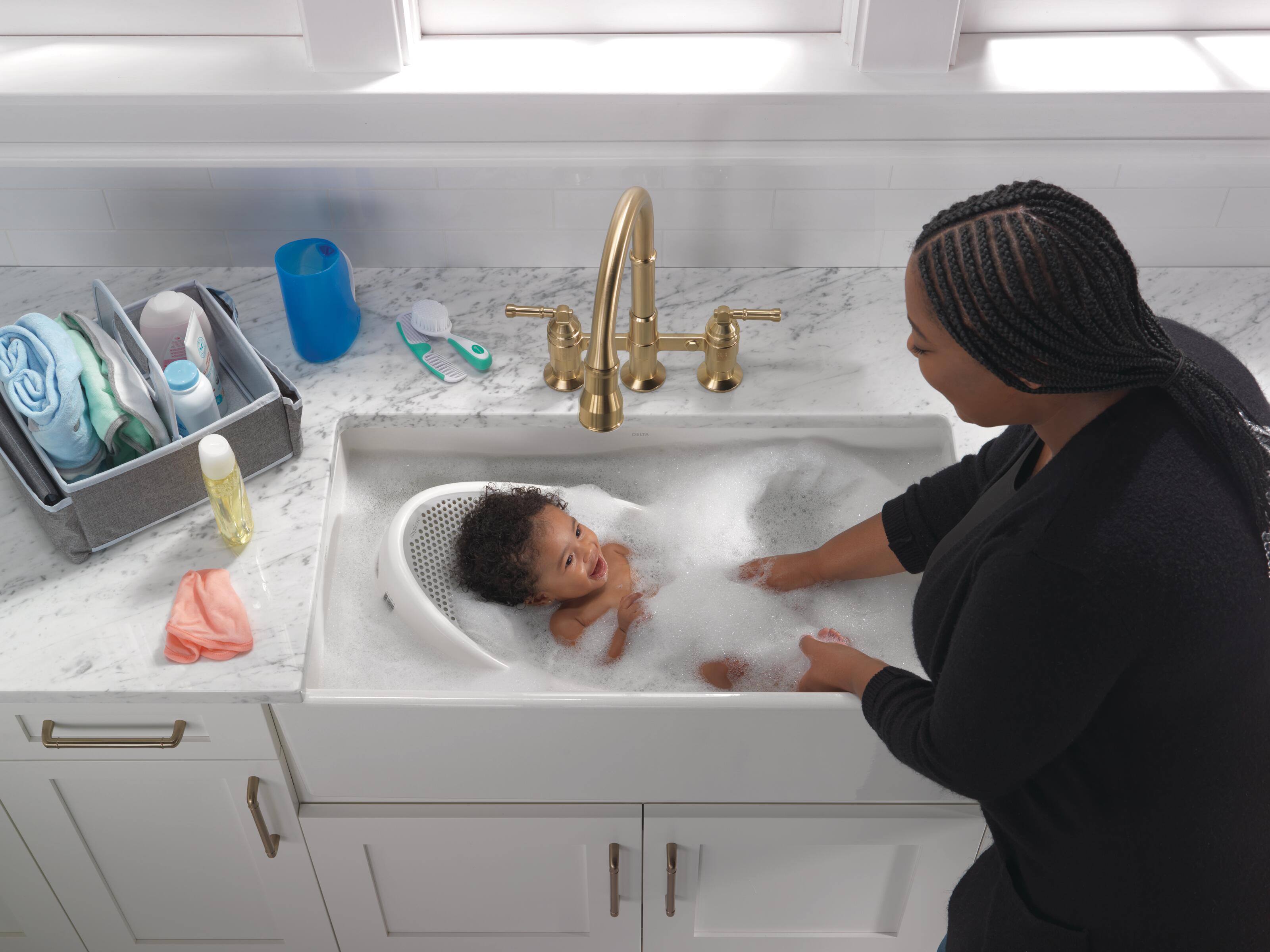 Mujer bañando a un bebé en el lavabo de la cocina con una llave Delta