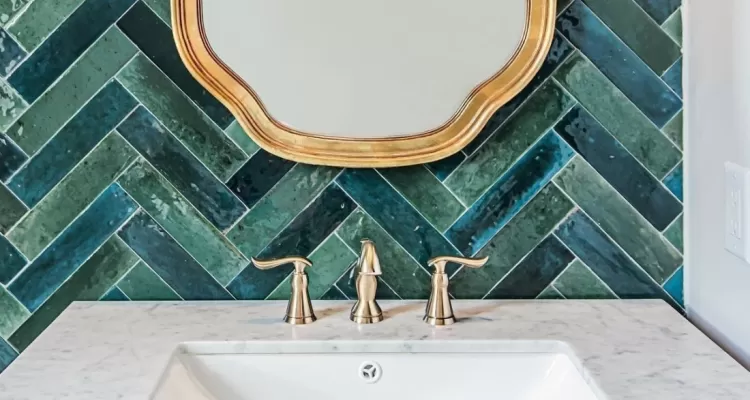 baño con azulejos con patrón de espinapez verde y detalles dorados