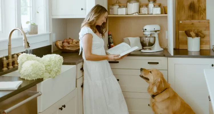 mujer lee un libro de cocina con el perro en la cocina