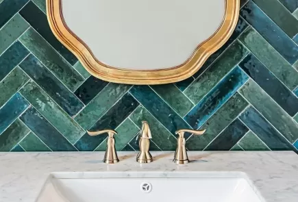 baño con azulejos con patrón de espinapez verde y detalles dorados