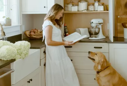 mujer lee un libro de cocina con el perro en la cocina